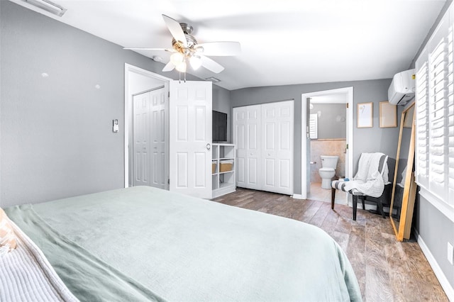 bedroom featuring lofted ceiling, ensuite bath, an AC wall unit, dark hardwood / wood-style floors, and ceiling fan