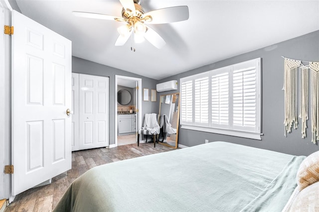 bedroom featuring ensuite bathroom, vaulted ceiling, an AC wall unit, hardwood / wood-style flooring, and ceiling fan