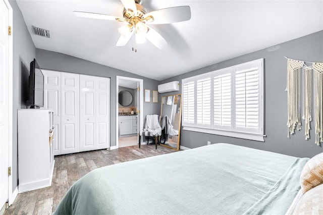 bedroom with ensuite bathroom, wood-type flooring, an AC wall unit, a closet, and ceiling fan