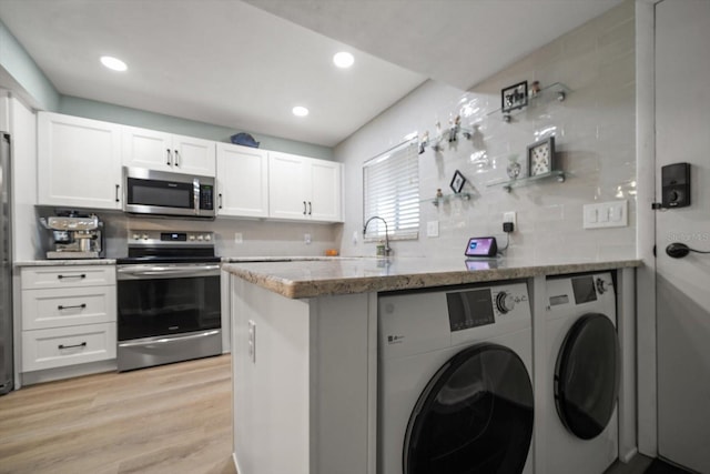 kitchen with appliances with stainless steel finishes, white cabinetry, dark stone counters, washing machine and clothes dryer, and light wood-type flooring