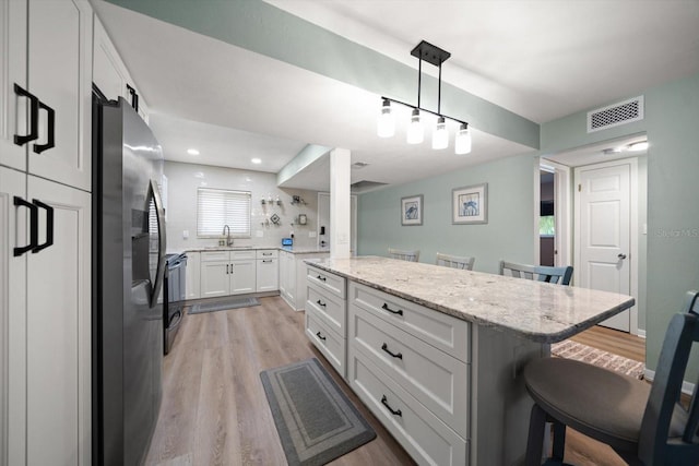 kitchen featuring sink, white cabinetry, a kitchen breakfast bar, light stone countertops, and stainless steel fridge with ice dispenser