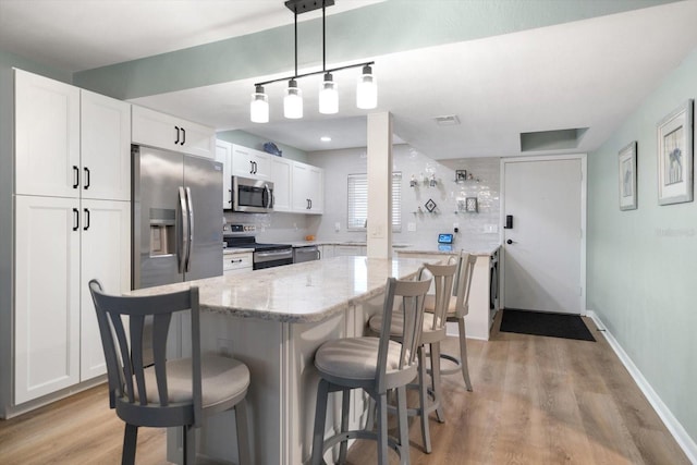 kitchen featuring stainless steel appliances, white cabinetry, a breakfast bar area, and decorative light fixtures