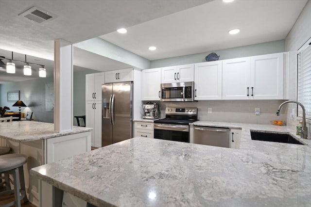 kitchen with sink, appliances with stainless steel finishes, a kitchen breakfast bar, light stone counters, and white cabinets