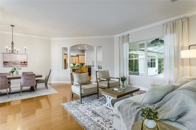 living room featuring crown molding, an inviting chandelier, light wood-type flooring, and ornate columns