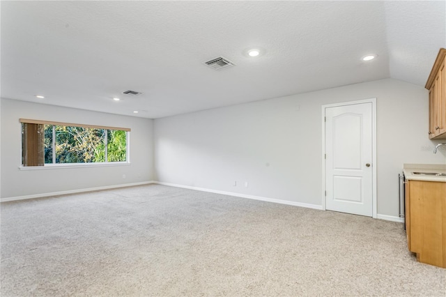 unfurnished living room with vaulted ceiling, sink, light colored carpet, and a textured ceiling