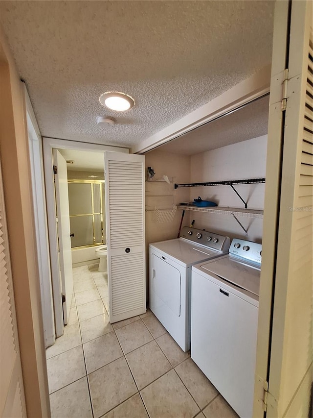 clothes washing area featuring light tile patterned flooring, washing machine and clothes dryer, and a textured ceiling