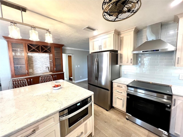 kitchen featuring hanging light fixtures, stainless steel appliances, ornamental molding, decorative backsplash, and wall chimney exhaust hood