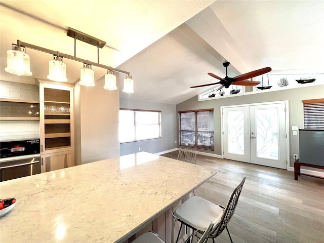 kitchen with light hardwood / wood-style flooring, a breakfast bar, lofted ceiling with beams, decorative light fixtures, and french doors