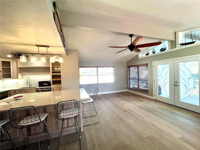 kitchen featuring pendant lighting, a breakfast bar area, vaulted ceiling with beams, backsplash, and light stone countertops