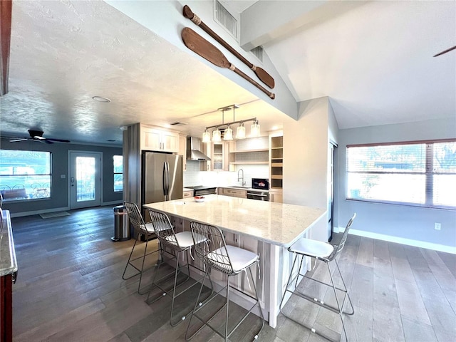 kitchen with pendant lighting, appliances with stainless steel finishes, a kitchen breakfast bar, dark hardwood / wood-style flooring, and wall chimney exhaust hood