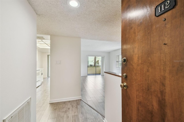 hall with a textured ceiling and light hardwood / wood-style floors