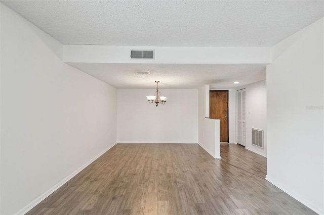 empty room featuring a notable chandelier, hardwood / wood-style flooring, and a textured ceiling