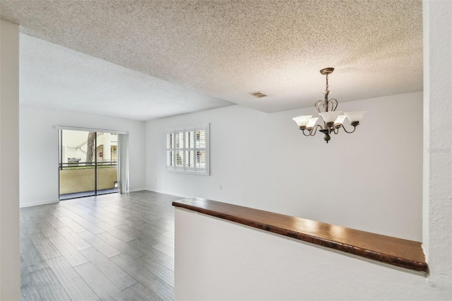 spare room with a notable chandelier, hardwood / wood-style flooring, and a textured ceiling