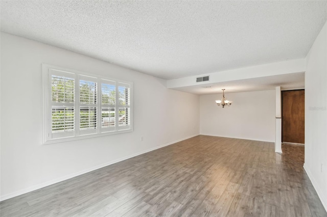 unfurnished room featuring hardwood / wood-style floors, a textured ceiling, and a notable chandelier