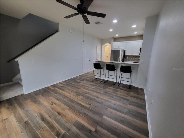 kitchen with dark wood-type flooring, stainless steel fridge, backsplash, white cabinets, and a kitchen bar