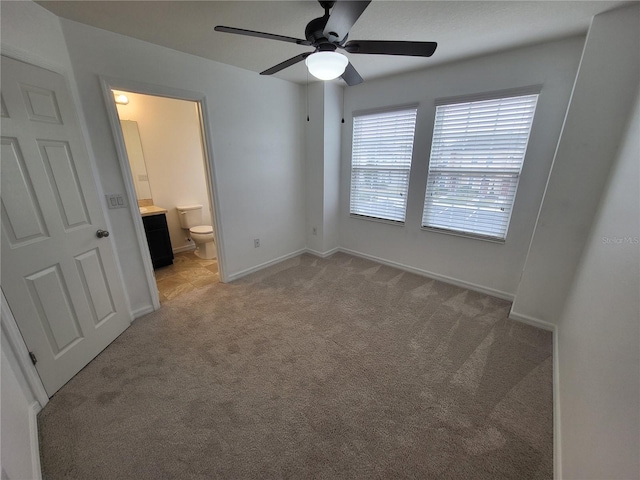 unfurnished bedroom featuring ceiling fan, ensuite bathroom, and light carpet