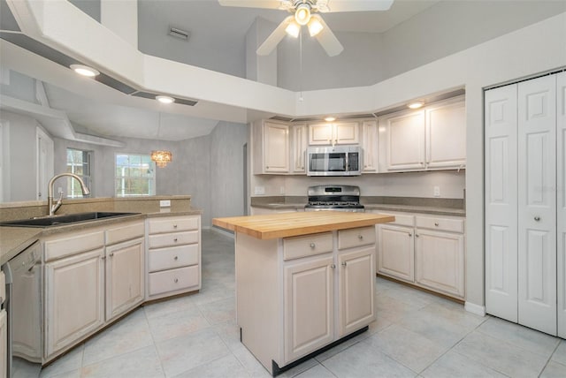 kitchen featuring sink, wooden counters, appliances with stainless steel finishes, a towering ceiling, and a center island