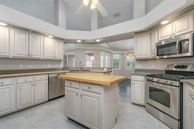 kitchen with sink, butcher block countertops, a center island, ceiling fan, and stainless steel appliances