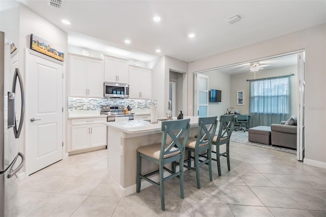 kitchen with a breakfast bar area, white cabinets, light tile patterned floors, stainless steel appliances, and a center island with sink