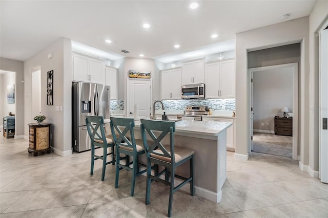 kitchen featuring white cabinetry, stainless steel appliances, a kitchen bar, and a kitchen island with sink