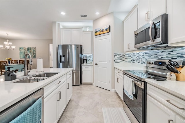 kitchen with pendant lighting, sink, appliances with stainless steel finishes, white cabinetry, and a chandelier