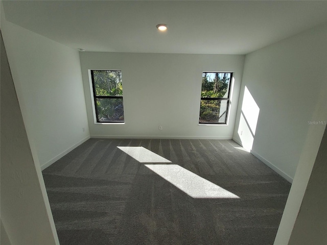 unfurnished room with plenty of natural light and dark carpet