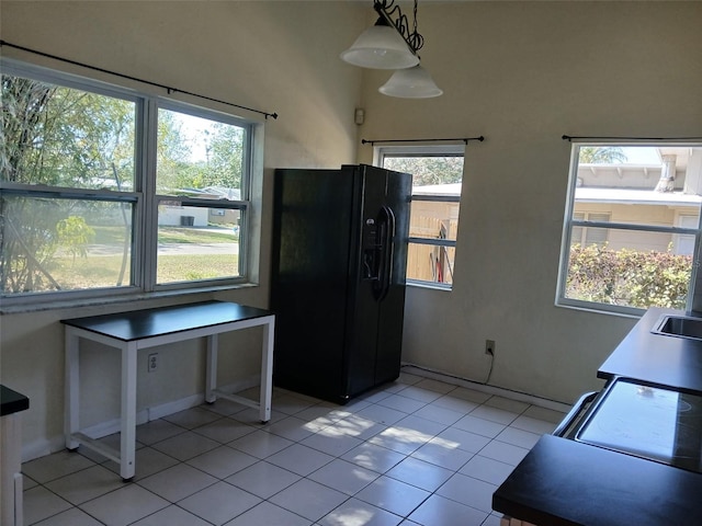 kitchen featuring black fridge, plenty of natural light, light tile patterned floors, and pendant lighting