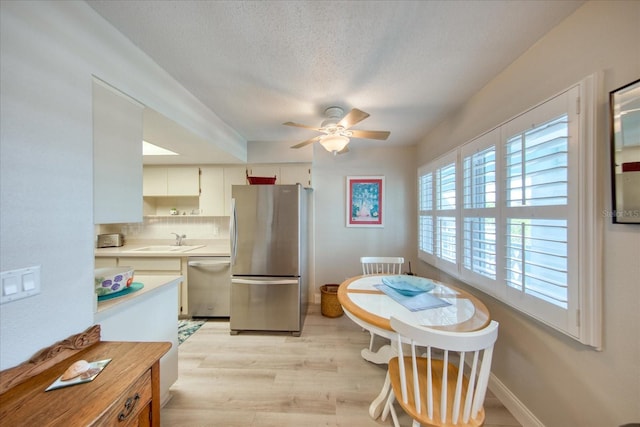 kitchen with sink, ceiling fan, backsplash, stainless steel appliances, and light hardwood / wood-style floors