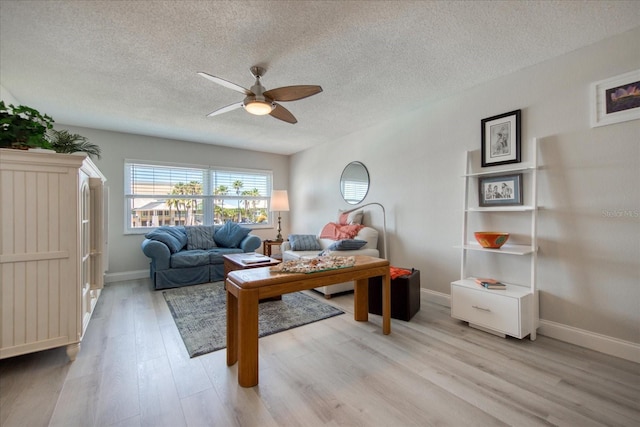 living room with a textured ceiling, ceiling fan, and light wood-type flooring