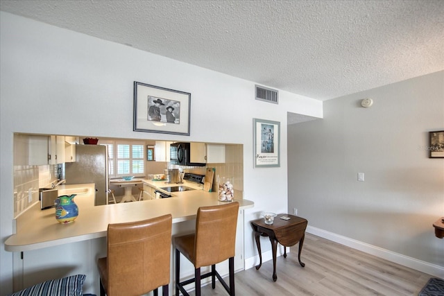 kitchen with a kitchen bar, light hardwood / wood-style flooring, kitchen peninsula, range with electric cooktop, and decorative backsplash