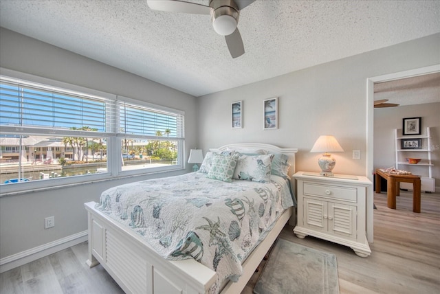 bedroom with a textured ceiling, ceiling fan, and light wood-type flooring