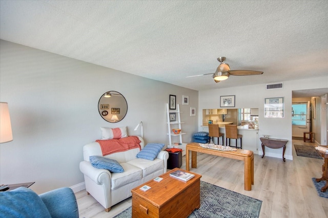 living room with ceiling fan, a textured ceiling, and light wood-type flooring