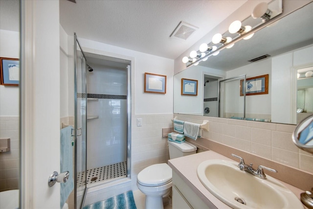 bathroom with a shower with shower door, tile walls, vanity, toilet, and a textured ceiling