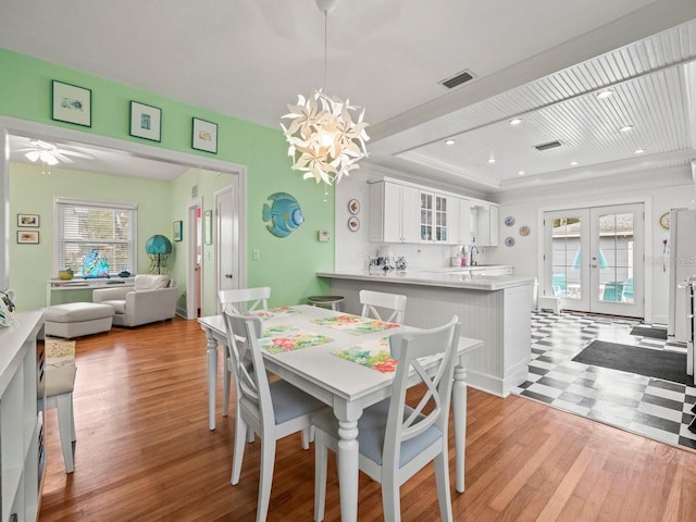 dining space with a raised ceiling, a chandelier, light hardwood / wood-style floors, and french doors