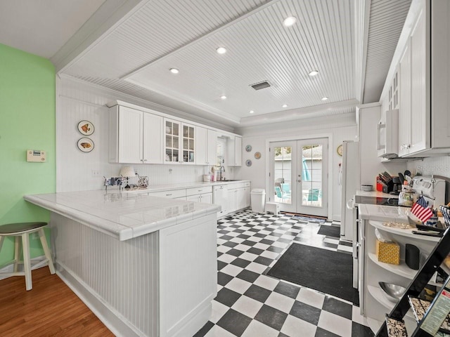 kitchen with a breakfast bar area, tile counters, white cabinets, french doors, and kitchen peninsula