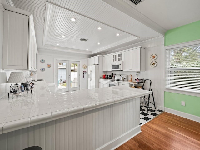 kitchen featuring white cabinets, tile counters, a raised ceiling, white appliances, and french doors