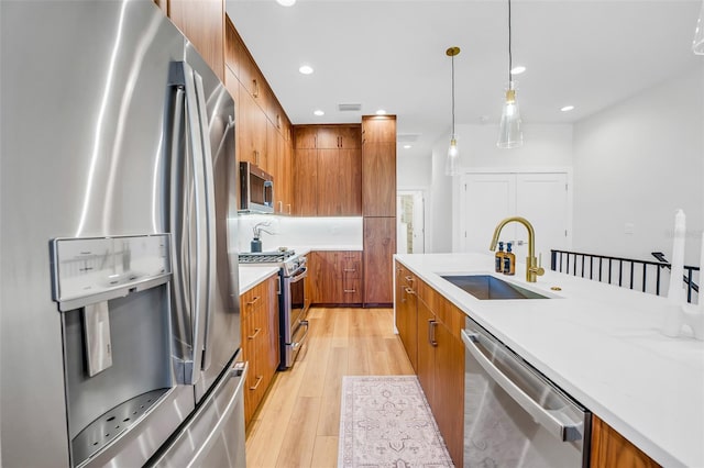 kitchen featuring stainless steel appliances, sink, light hardwood / wood-style floors, and decorative light fixtures