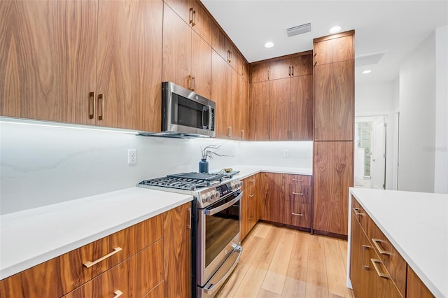 kitchen with appliances with stainless steel finishes, light hardwood / wood-style floors, and backsplash