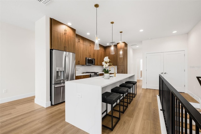 460 87th Ave N, Saint Petersburg, FL 33702 - kitchen with light countertops, light wood-style flooring, a kitchen breakfast bar, appliances with stainless steel finishes, and brown cabinetry