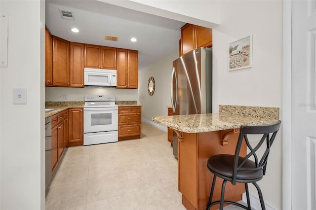 kitchen featuring light tile patterned floors, white appliances, a kitchen breakfast bar, light stone counters, and kitchen peninsula