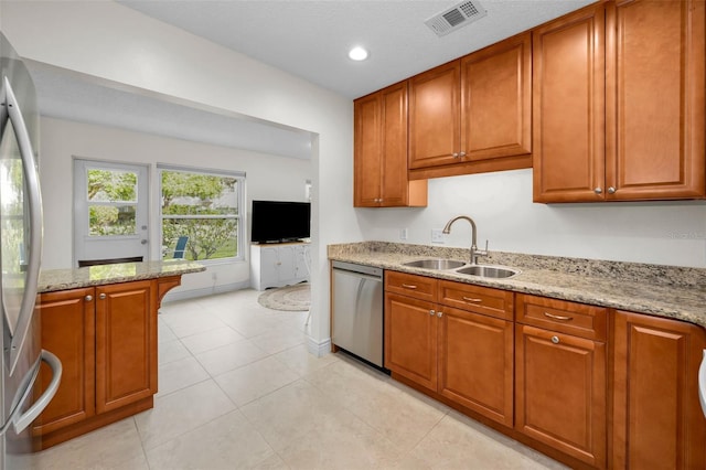 kitchen with sink, a textured ceiling, light tile patterned floors, stainless steel appliances, and light stone countertops