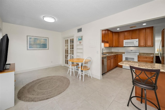 kitchen with sink, light tile patterned floors, white appliances, light stone countertops, and a textured ceiling