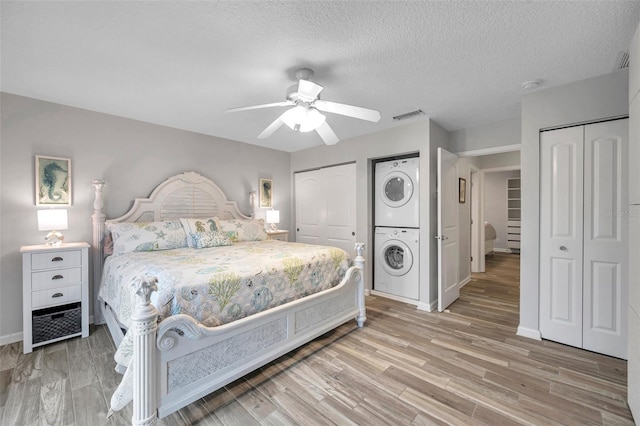 bedroom featuring stacked washer and dryer, a textured ceiling, light wood-type flooring, two closets, and ceiling fan