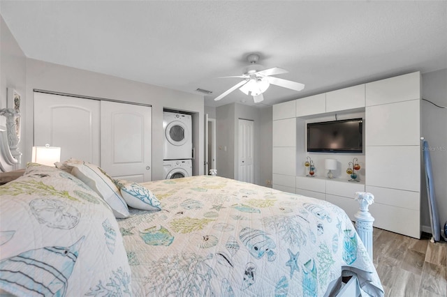 bedroom with stacked washer / drying machine, multiple closets, light hardwood / wood-style floors, and ceiling fan