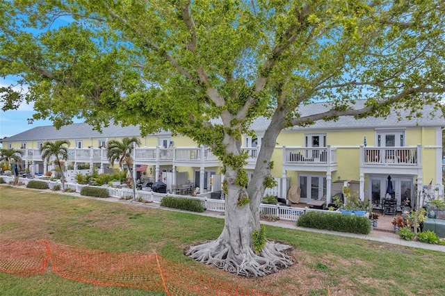 exterior space featuring a balcony, a front lawn, and a patio