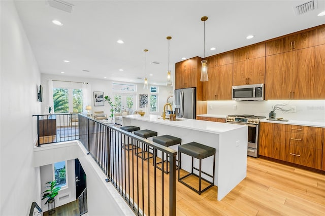 kitchen with an island with sink, a kitchen breakfast bar, hanging light fixtures, light hardwood / wood-style floors, and stainless steel appliances