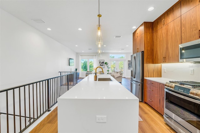 kitchen featuring pendant lighting, sink, stainless steel appliances, a center island with sink, and light wood-type flooring