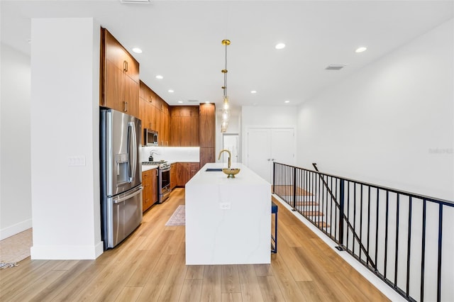 kitchen featuring decorative light fixtures, sink, stainless steel appliances, a center island with sink, and light wood-type flooring