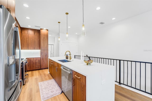 kitchen featuring sink, light hardwood / wood-style flooring, a kitchen island with sink, stainless steel appliances, and decorative light fixtures