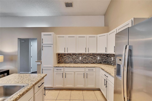 kitchen featuring white cabinetry, stainless steel refrigerator with ice dispenser, light stone counters, and decorative backsplash